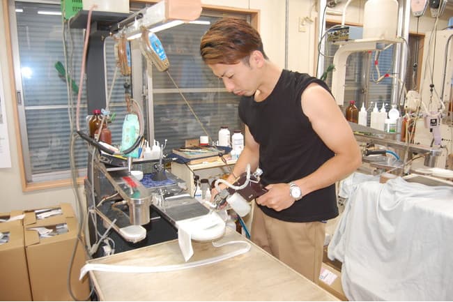 作業台でスプレー機を用い、布地のしみ抜き作業に集中する職人の様子